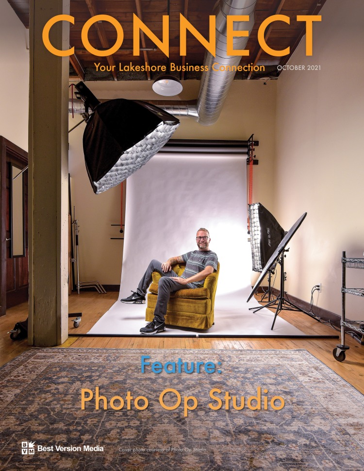 The cover of the October 2021 issue of CONNECT magazine. A photo backdrop with lights and equipment, focused on a smiling man sitting sideways in a velvet, mustard-colored armchair. He looks quirky, humble, and relaxed. Text reads: "Feature: Photo Op Studio"